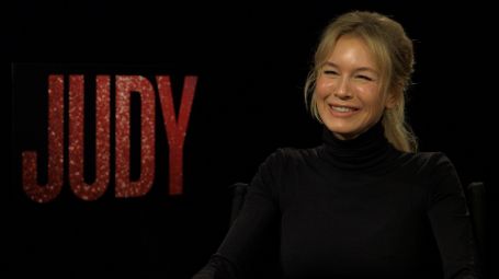 rene sitting on a chair smiling infront of a back drop which says 'judy'